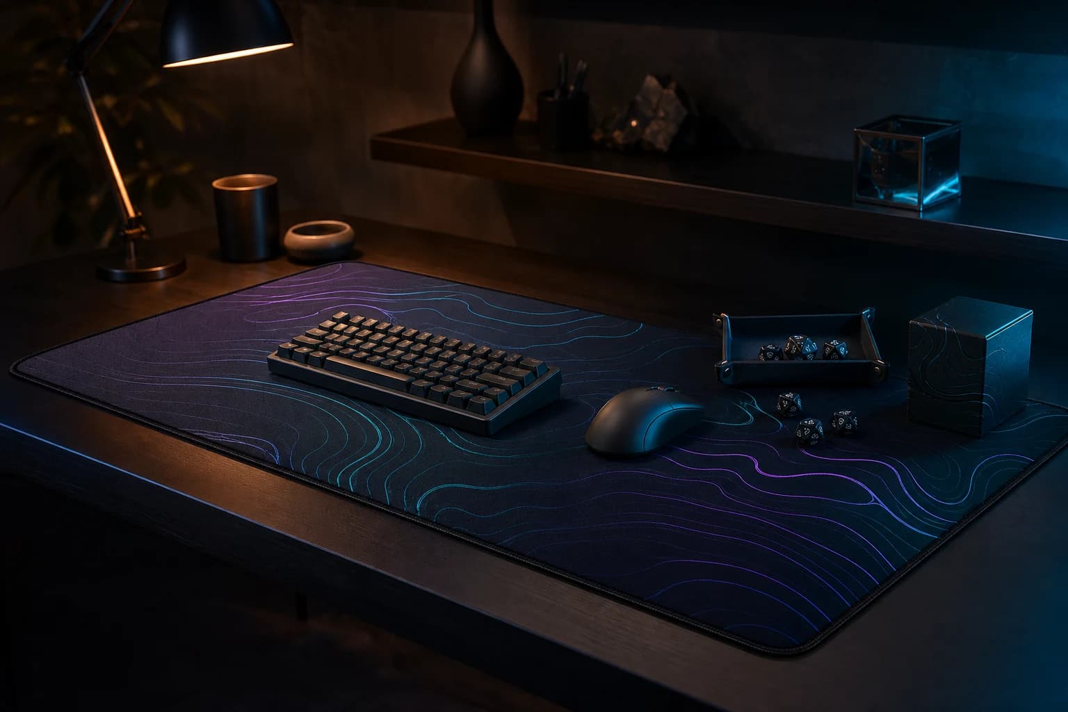 A dark desk mat with cyan and violet contour artwork, set with a keyboard, mouse, dice tray and deck box