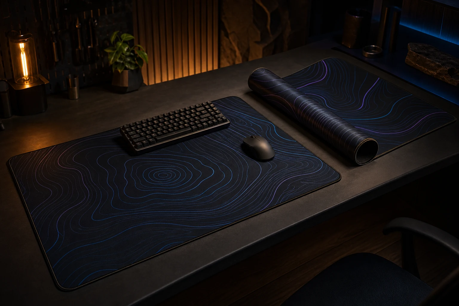 Two dark stitched desk mats with subtle cyan and violet contour patterns on a dark desk.